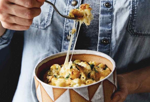 A man with a forkful of Anaheim green chile macaroni and cheese over a bowl of the same, with strands of Cheddar and Monterey Jack cheeses