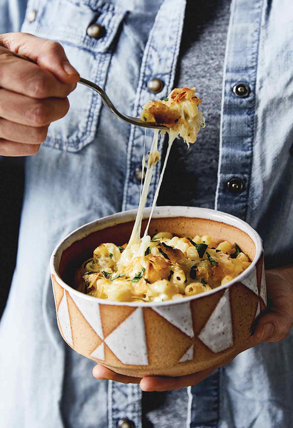 A man with a forkful of Anaheim green chile macaroni and cheese over a bowl of the same, with strands of Cheddar and Monterey Jack cheeses