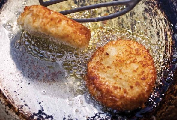 Old frying pan with two leftover mashed potato cakes being turned by a spatula
