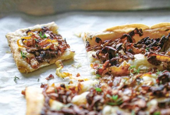 A sheet pan with an onion thyme tart on it, covered with cooked onions, thyme on a puff pastry crust