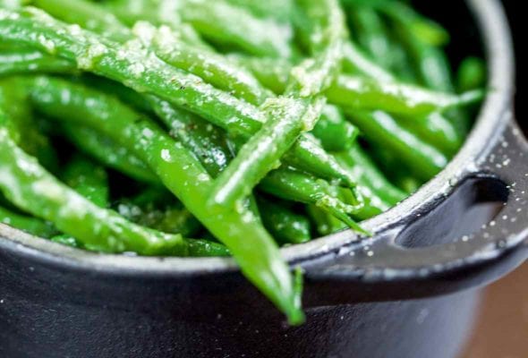 A cast-iron pot filled with pan-fried green beans tossed with garlic and butter