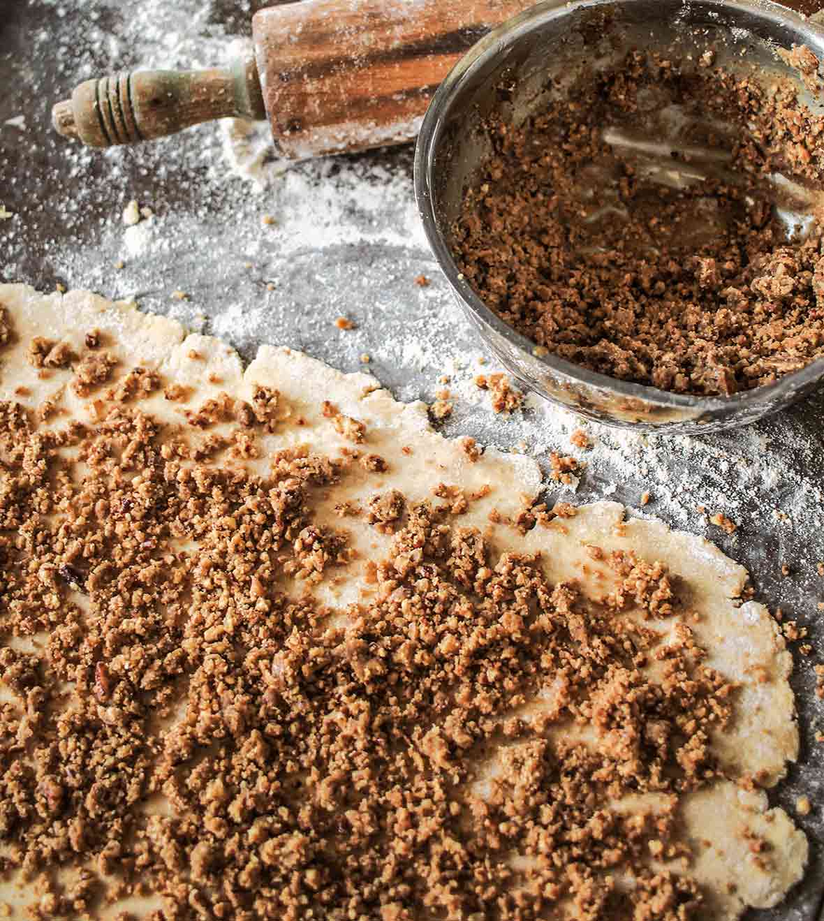 Rugelach dough covered with pecan pie filling and a bowl of filling nearby