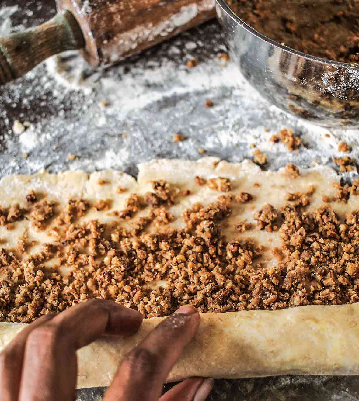 Rugelach dough covered with pecan pie filling being rolled up and a bowl of filling nearby