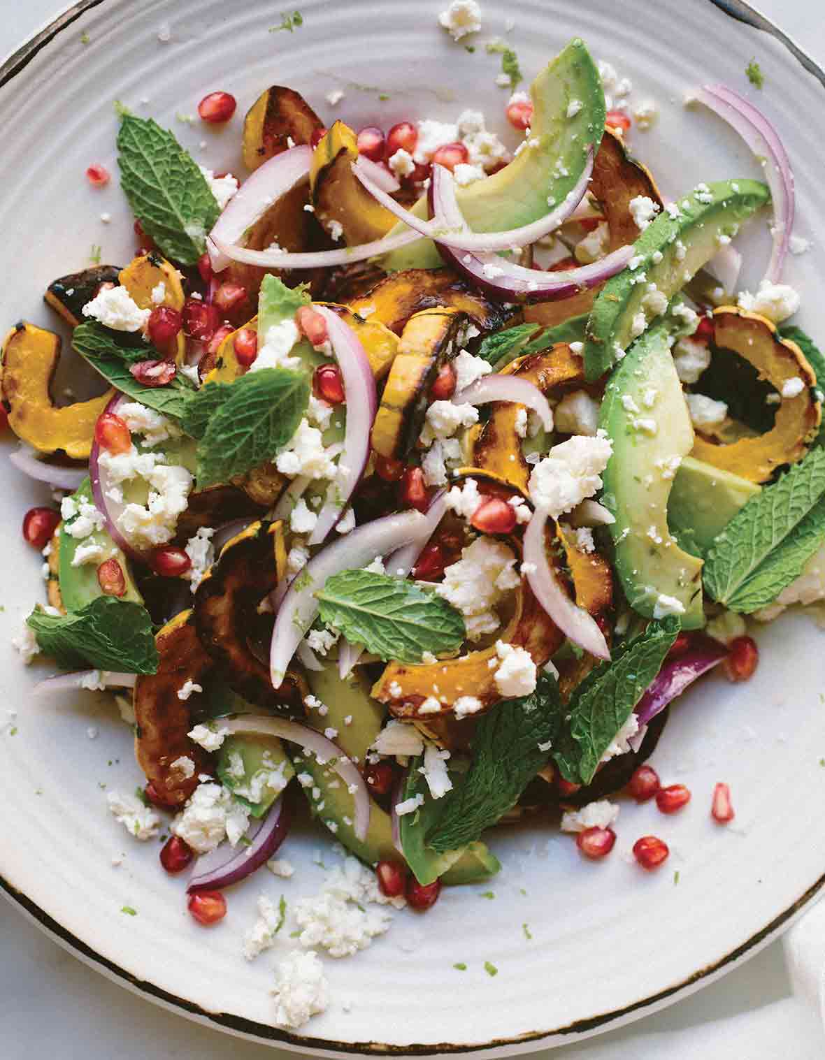 A plate of roasted delicata squash salad with red onion, feta cheese, avocado, and mint