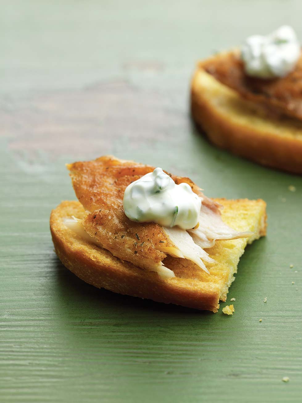 Two smoked trout crostini--toasted rustic bread with a flack of smoked trout and sour cream--on green wood table