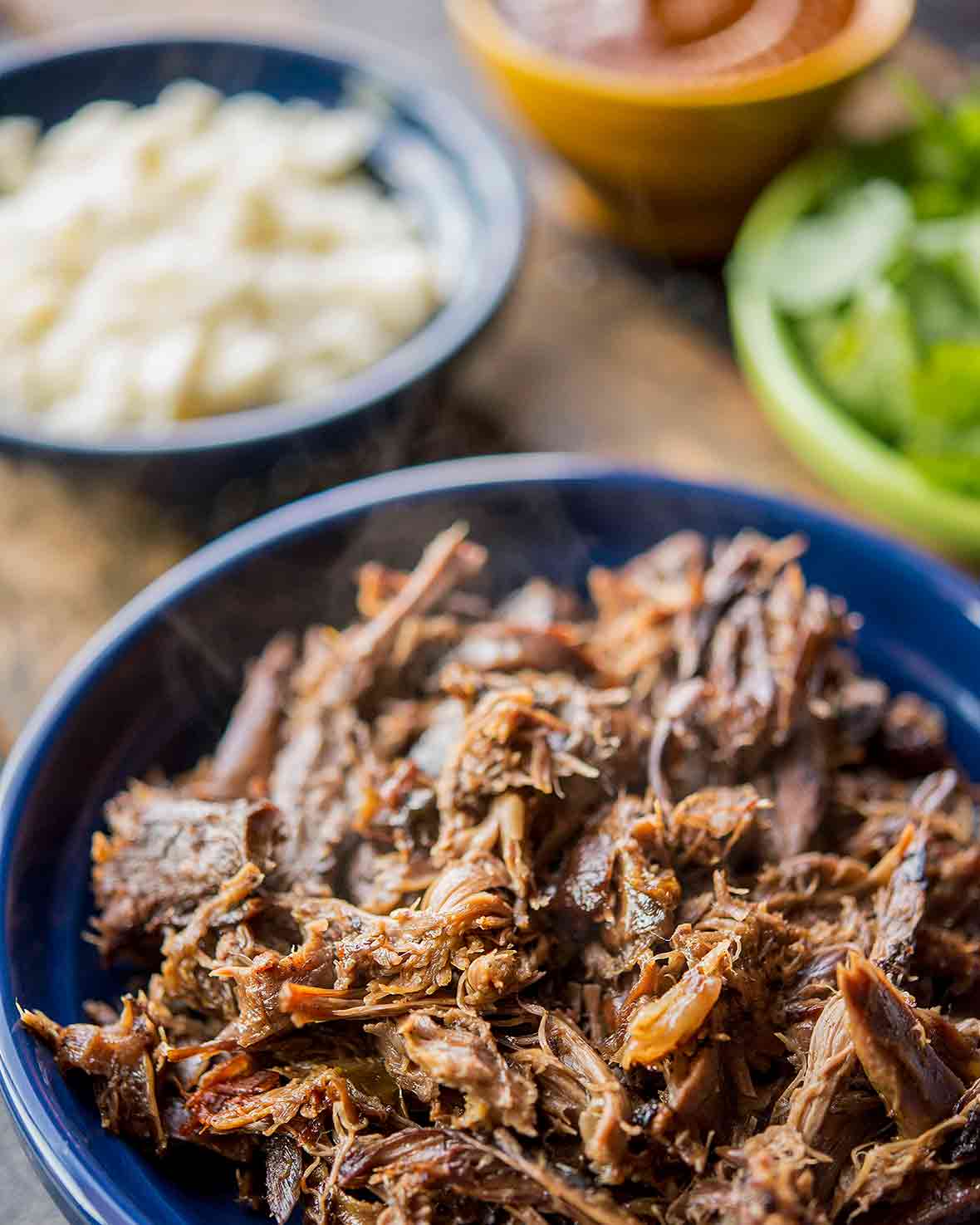 A blue bowl of shredded turkey leg barbacoa braised with flavored with bay leaves, paprika, cumin, cloves, oregano, lime juice, vinegar