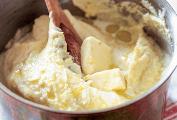 A pot of smooth mashed potatoes--made with plenty of butter, cream--with a wooden spoon and pat of butter on top