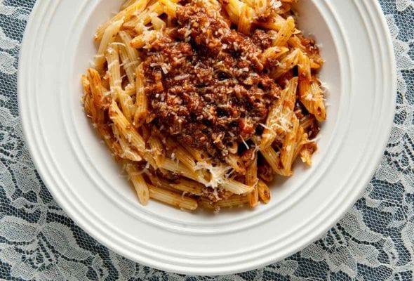 White bowl of venison Bolognese made with ground venison, carrots, onion, celery, mushrooms a top rigatoni