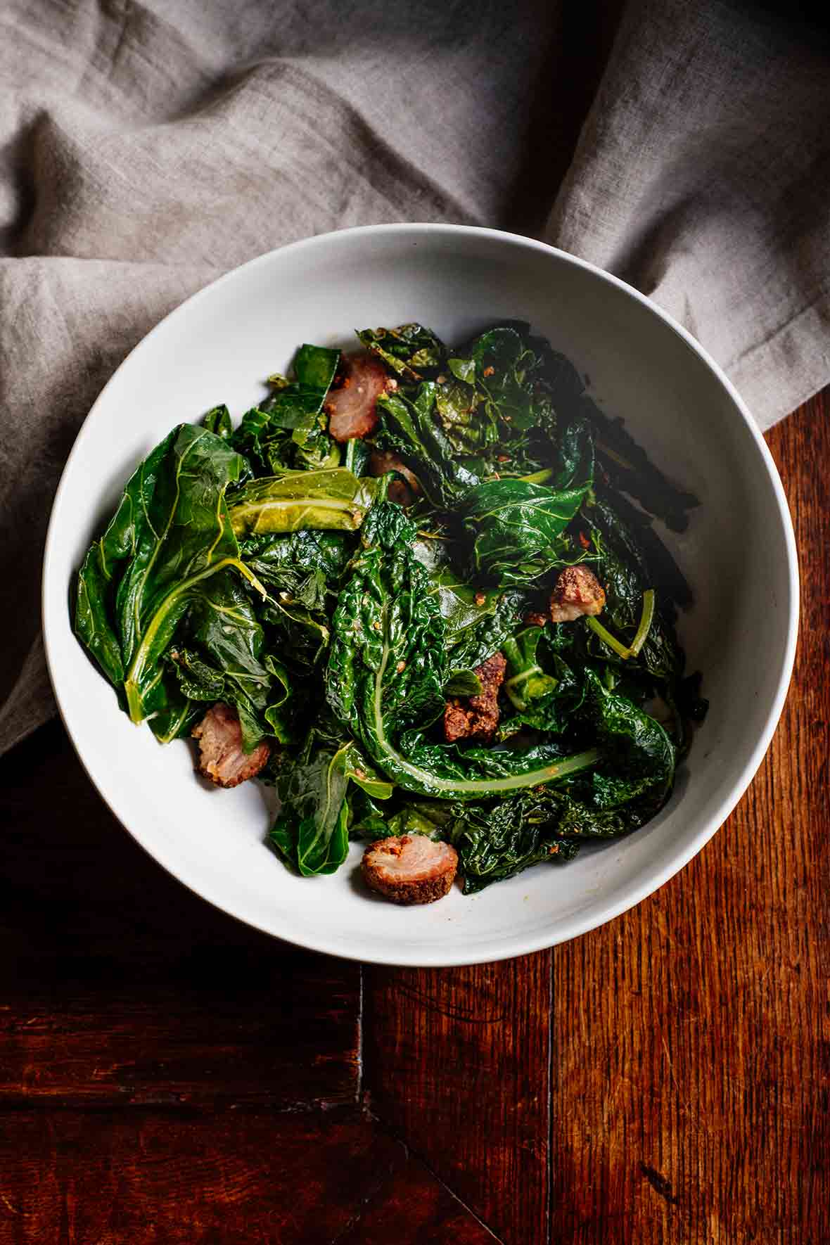A bowl of braised greens--spinach, kale, collards--and chunks of andouille sausage