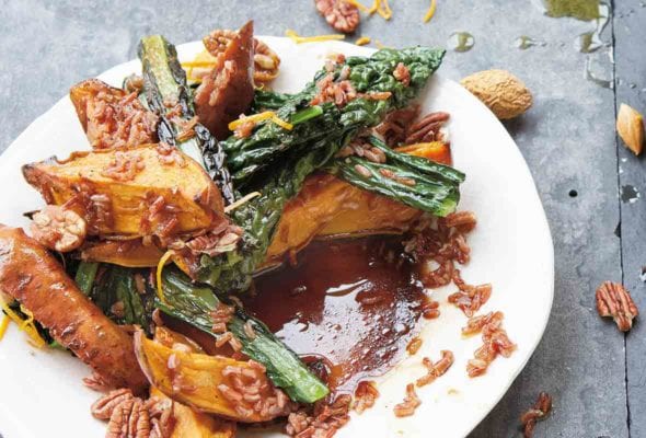 A white plate with a messy sweet potato, kale, rice, and pecan salad