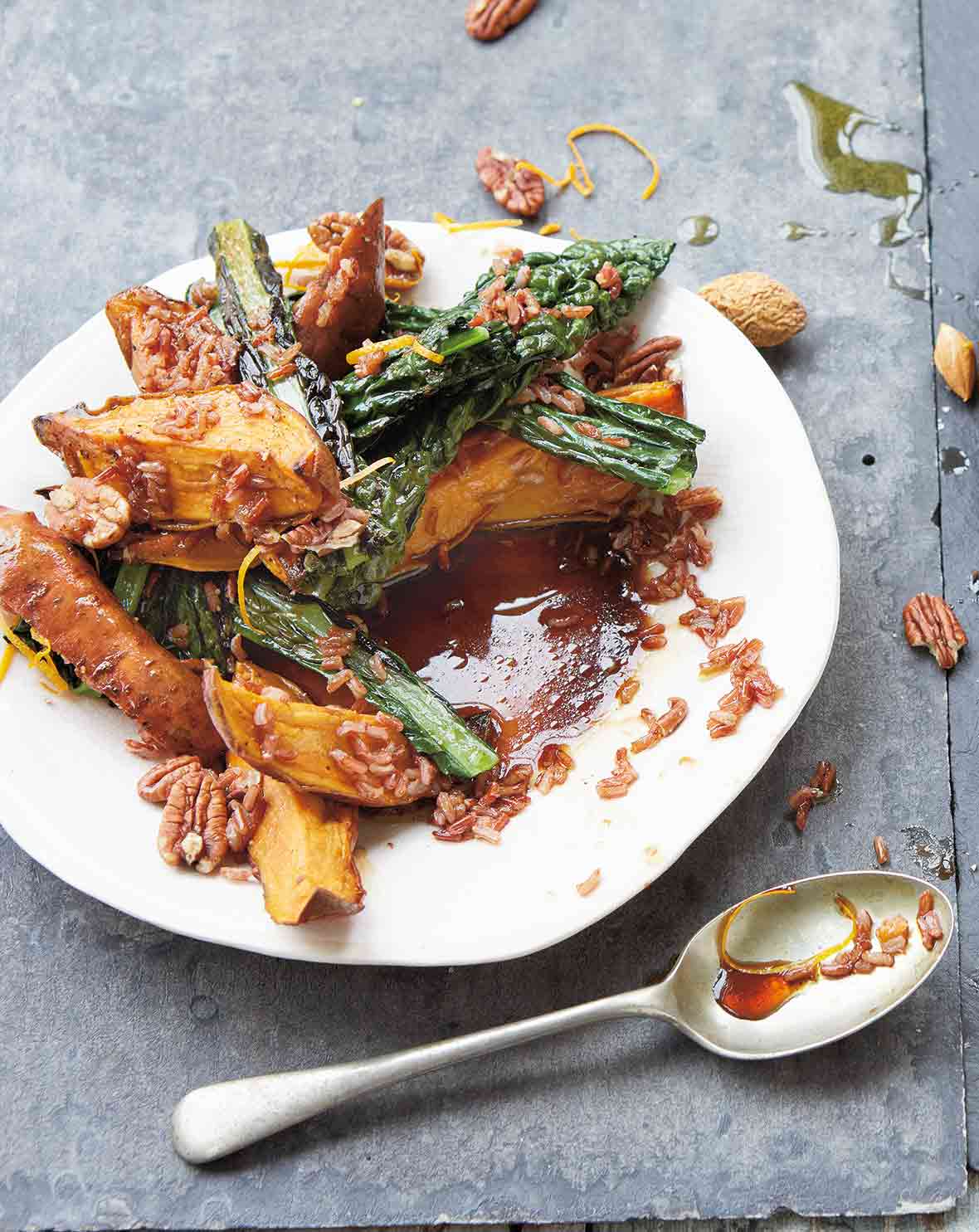 A white plate with a messy sweet potato, kale, rice, and pecan salad