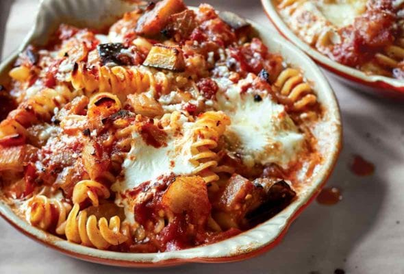 Three ceramic dishes with baked pasta with tomatoes and eggplant and sprinkled with Parmesan cheese