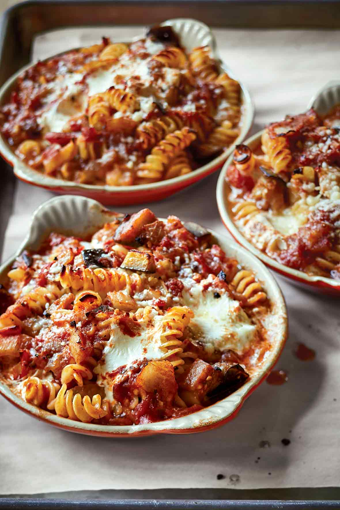 Three ceramic dishes with baked pasta with tomatoes and eggplant and sprinkled with Parmesan cheese