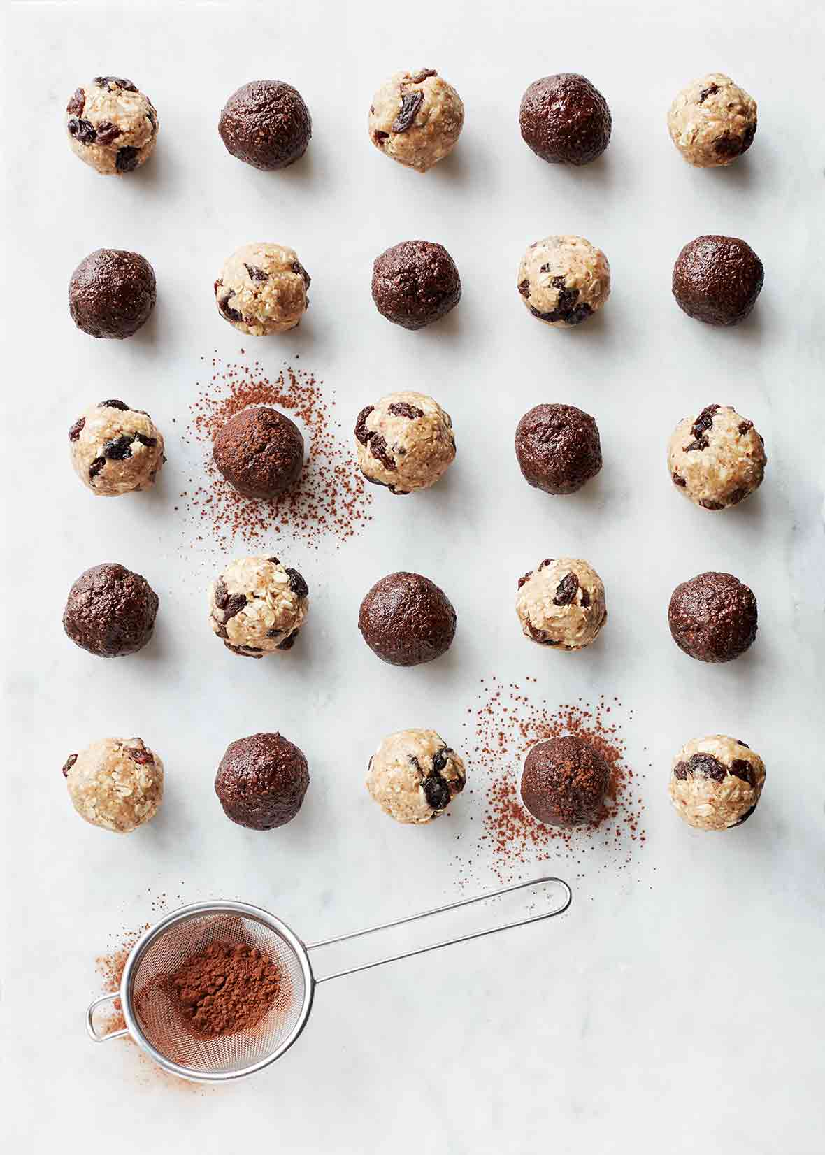 25 chocolate energy balls, made with dates, almond butter, almonds, and cacao powder, on white marble