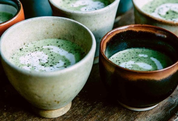 Four handmade bowls of green-speckled creamy broccoli soup with feta