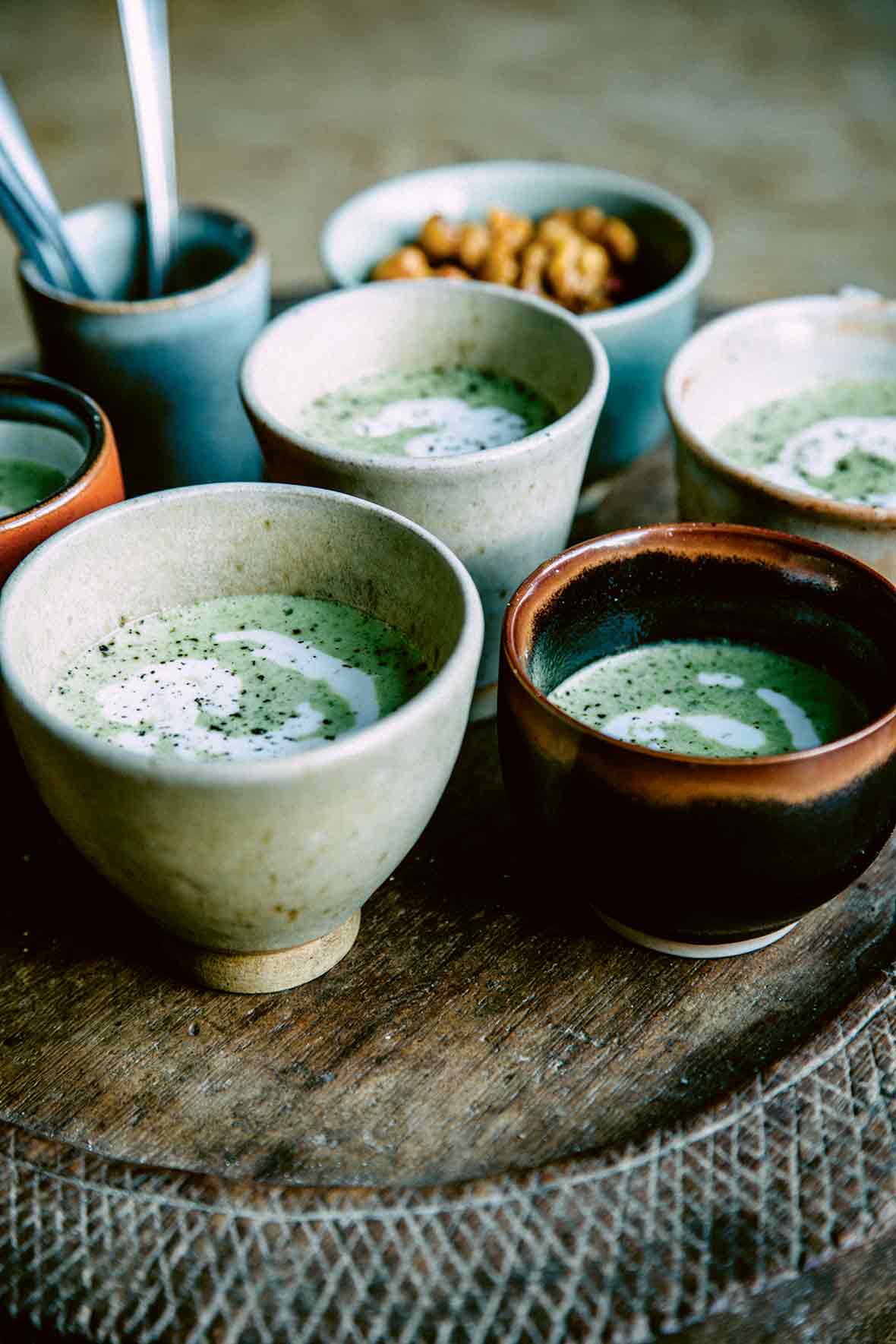 Four handmade bowls of green-speckled creamy broccoli soup with feta