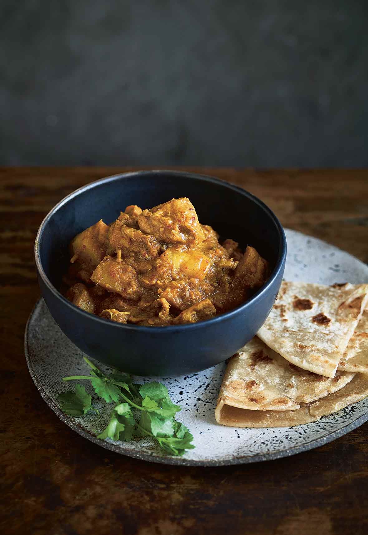 A bowl of devil's curry--chunks of chicken thighs, potatoes, and curry paste with naan bread on the side