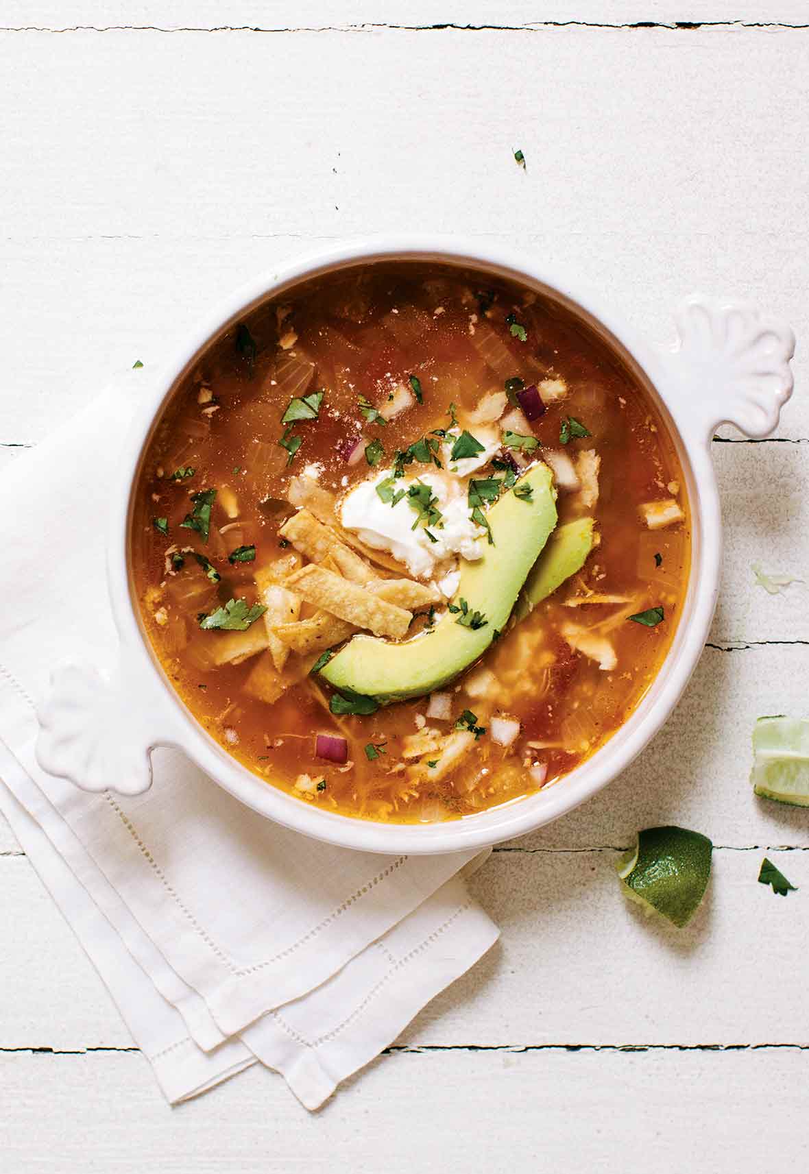 A bowl of easy chicken tortilla soup, with chicken, avocado, tortilla strips, and sour cream