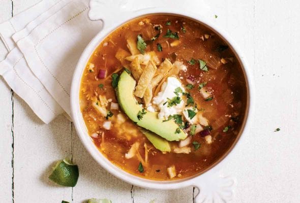 A bowl of easy chicken tortilla soup, with chicken, avocado, tortilla strips, and sour cream