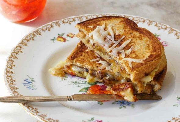 A grilled cheese sandwich with peppers is cut in half and stacked on a china plate with a jar of pepper jelly on the side