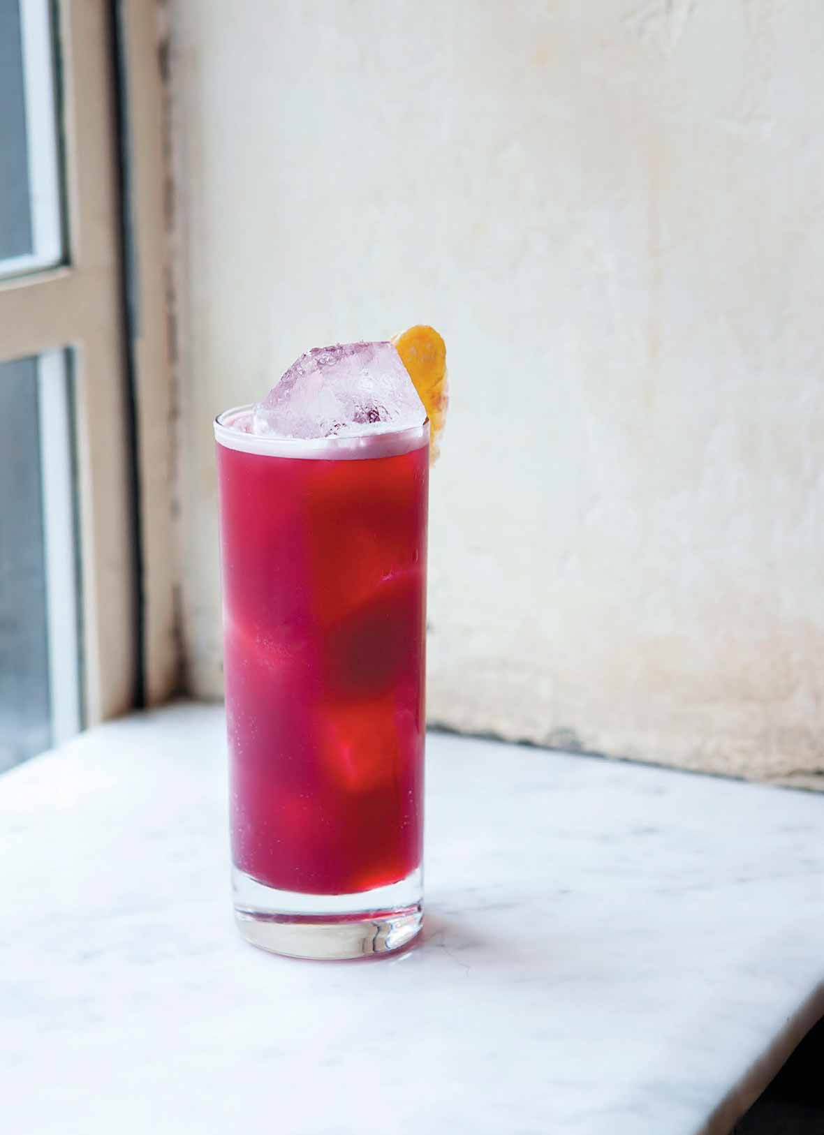 A tall, cool pink Kitty highball, filled with ice, and sporting a lemon slice