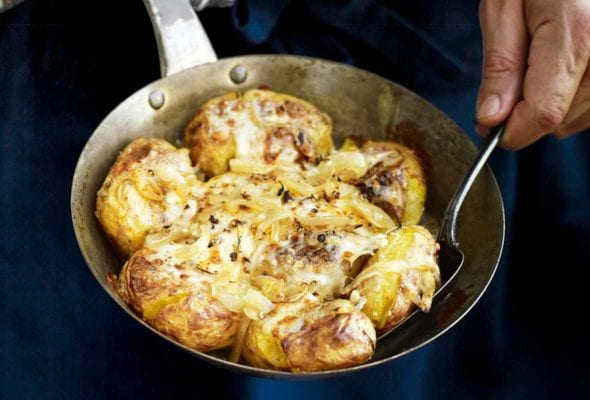 A man with a skilet of Portuguese punched potatoes, caramelized onions, cheese, called batatas a murro in Portuguese