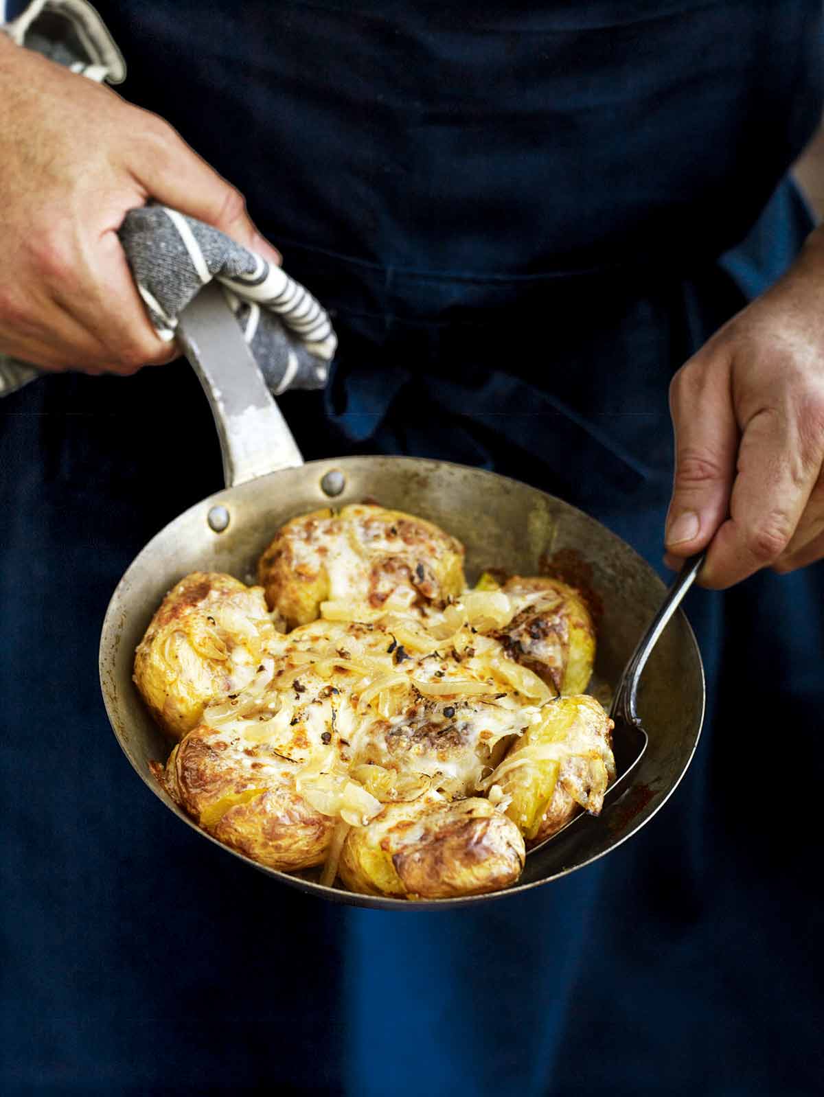 A man with a skilet of Portuguese punched potatoes, caramelized onions, cheese, called batatas a murro in Portuguese