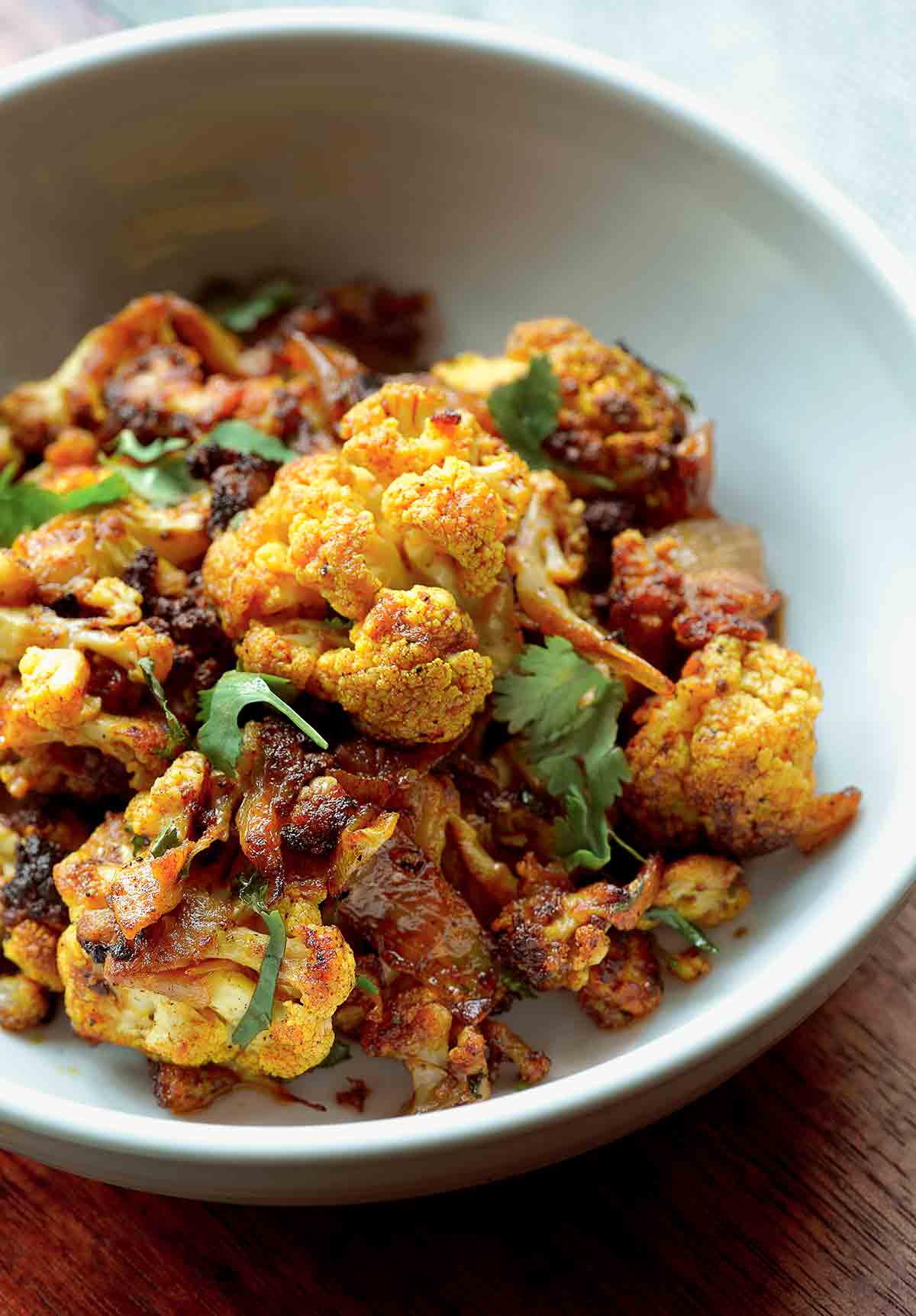 A bowl of roasted curried cauliflower mixed with onions and topped with cilantro