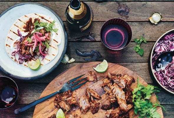 A shredded beef taco bar--a wooden platter with a braised beef shank, cilantro, lime, and pickled onions