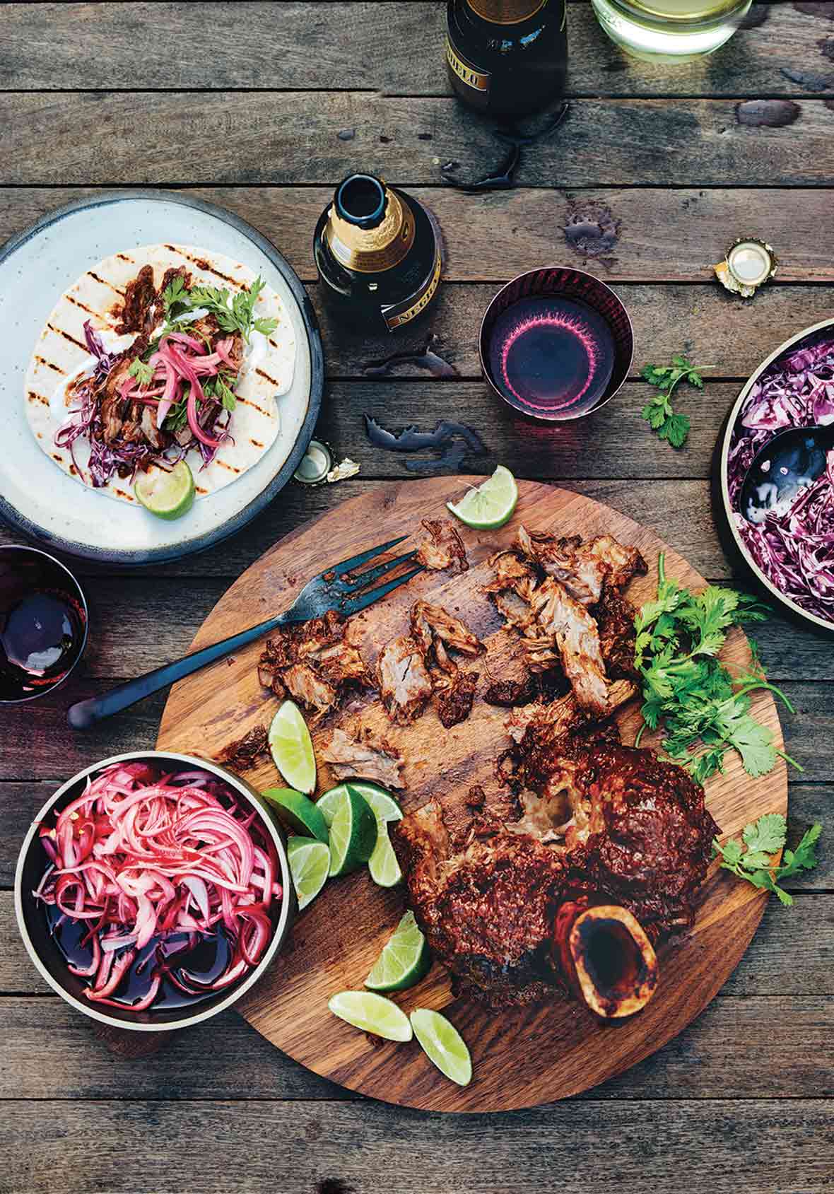 A shredded beef taco bar--a wooden platter with a braised beef shank, cilantro, lime, and pickled onions