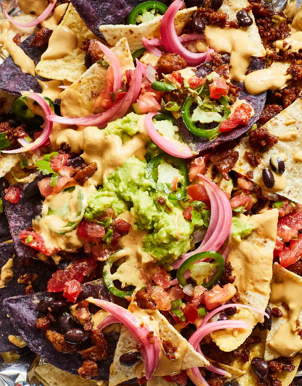 A close up of vegan nachos made with seitan, plus a sour lime cream, cashew, pickled red onions, avocado, jalapeño, and cilantro