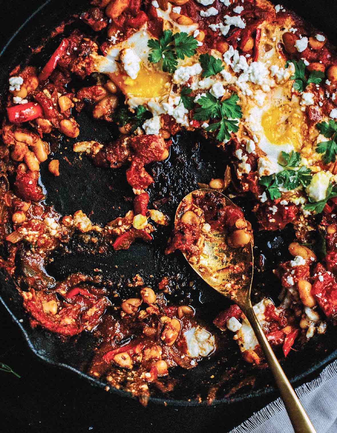 Cast iron skillet with white bean shakshuka--whit beans, tomatoes, feta cheese, eggs, and parsley
