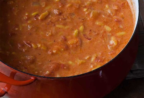 A large pot of easy tomato soup with a grilled cheese sandwich being cut into croutons beside it.
