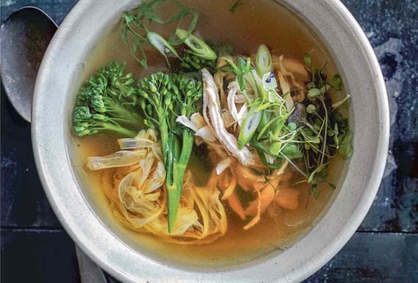 A bowl of healthy egg drop soup with shredded chicken, green onions, broccoli rabe, noodles, and sprouts