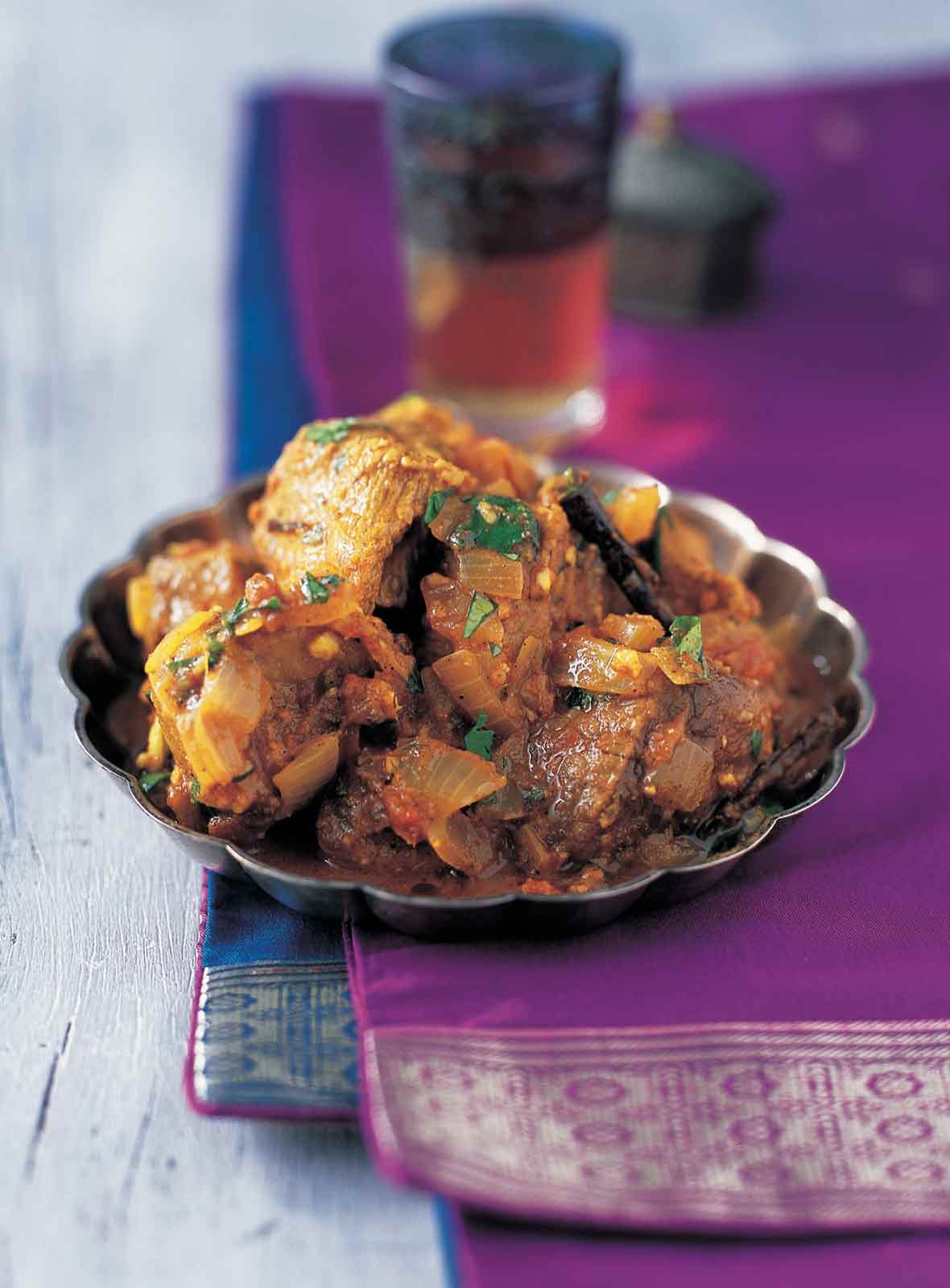 A scalloped metal plate filled with lamb curry and sprinkled with cilantro