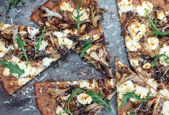 A mushroom and goat cheese pizza topped with dandelion leaves cut into six slices