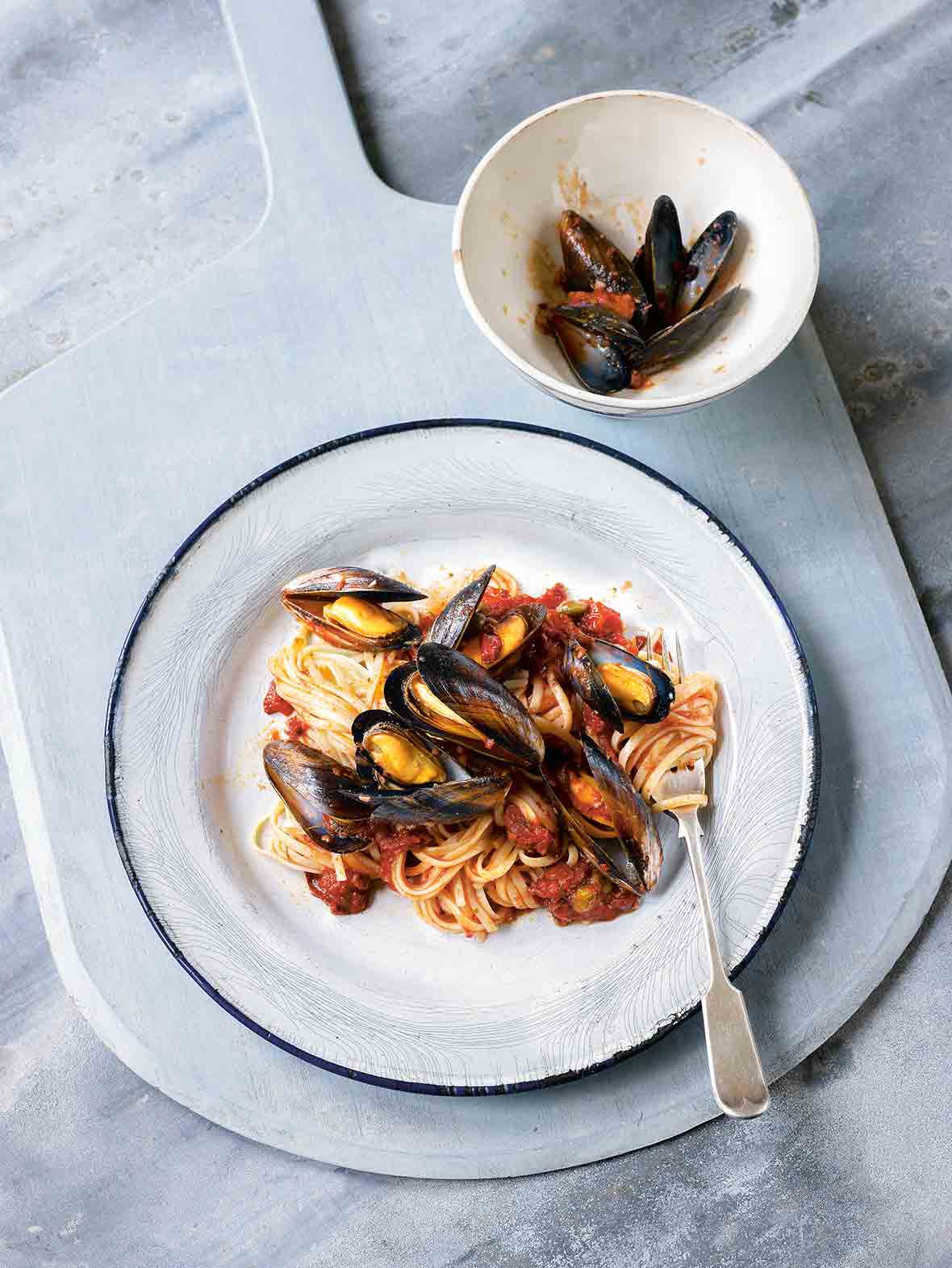 A white plate topped with linguine and mussels in a red dress