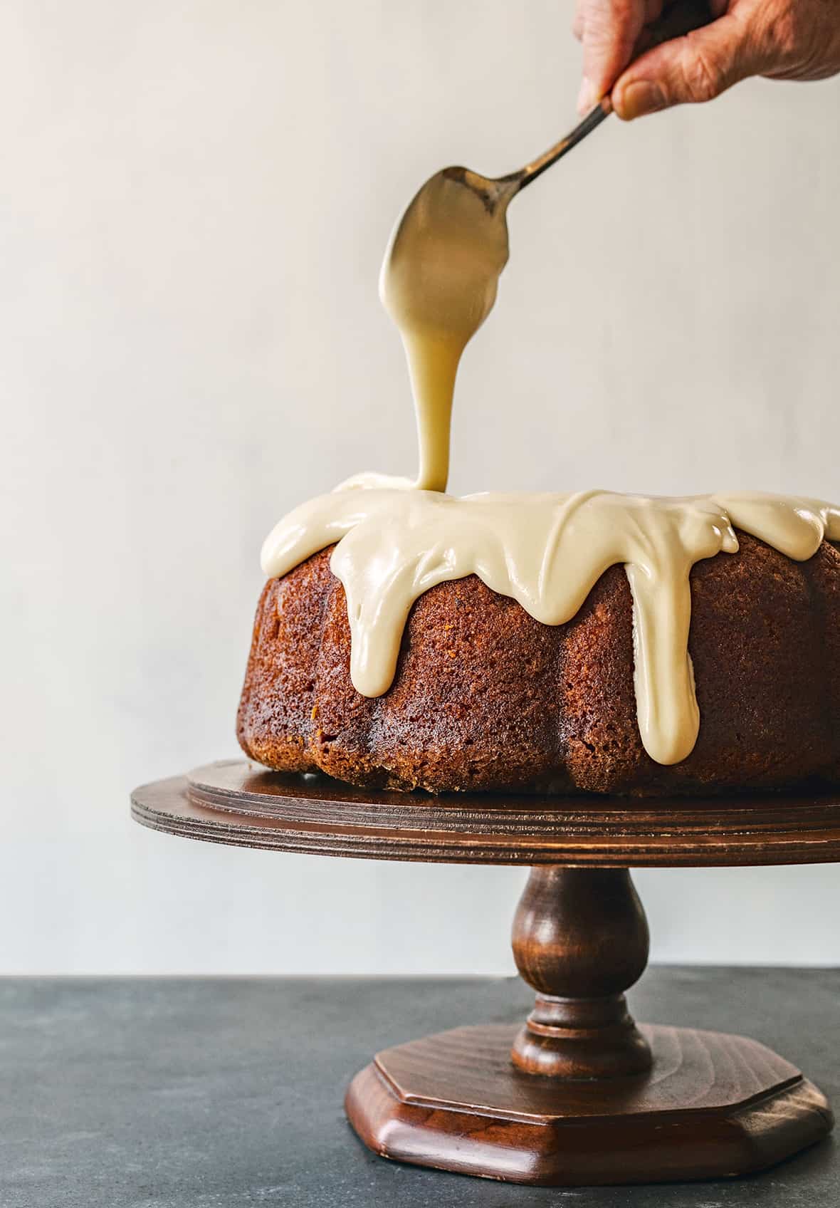 A Red Truck Bakery apple cake on a cake stand being drizzled with maple glaze