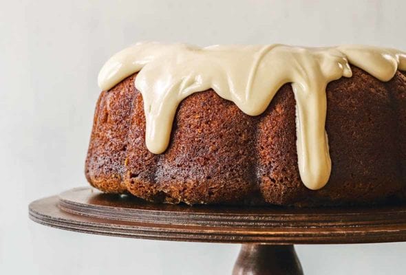 A Red Truck Bakery apple cake on a cake stand being drizzled with maple glaze