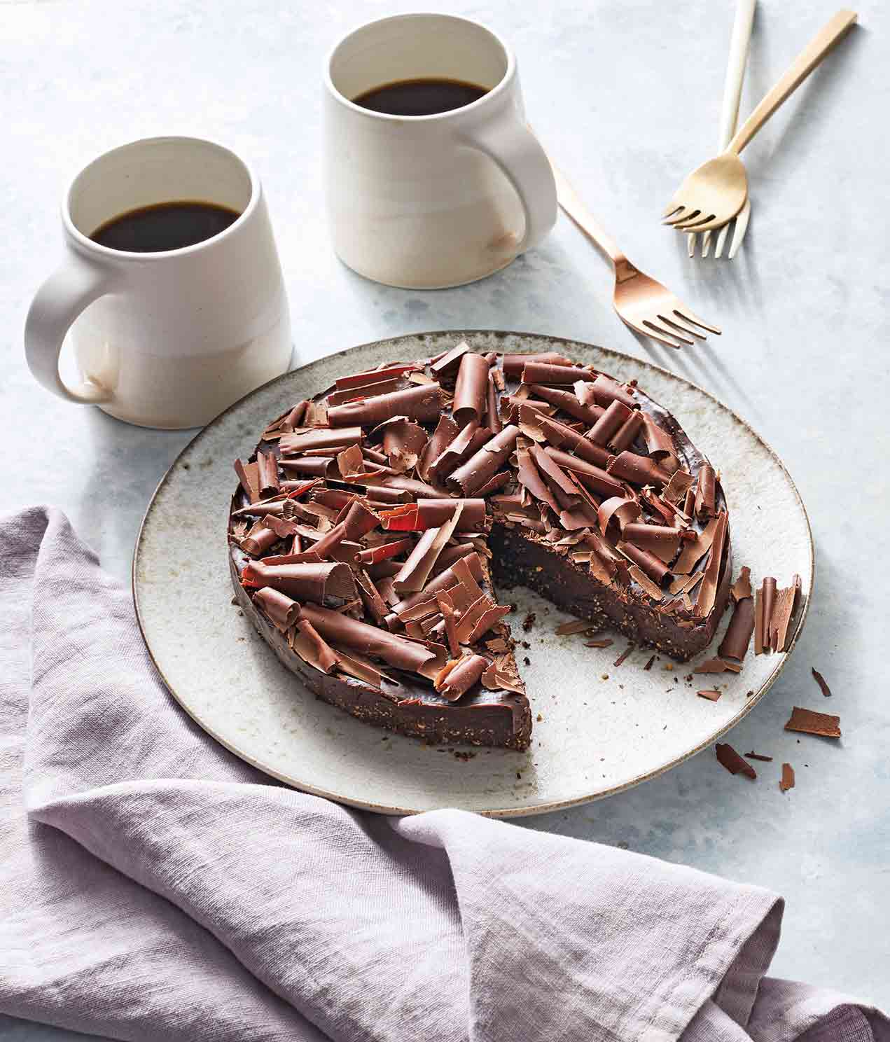 Two mugs of coffee and a white plate with a vegan no-bake fudge cake