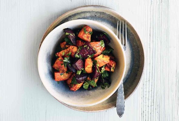 An earthenware bowl filled with curried butternut squash and beets, on a plate with a fork resting beside the bowl