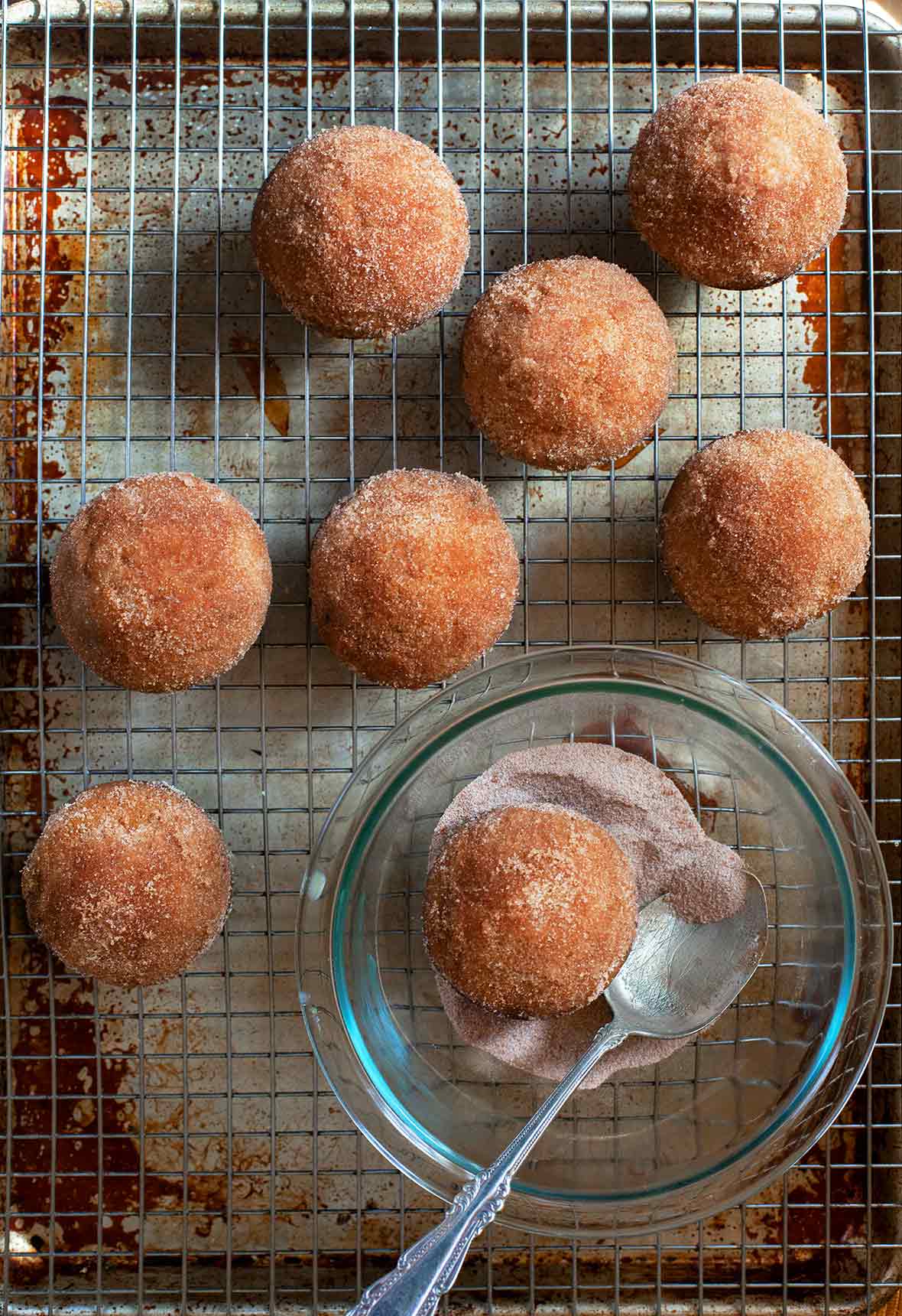 Seven dirt bombs cooling on a wire rack, and one in a bowl of cinnamon sugar