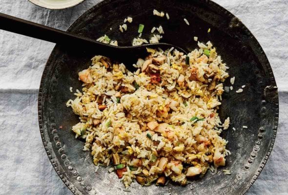 A decorative metal serving bowl filled with fried rice with leftovers and a bowl of jalapeño garlic vinegar on the side