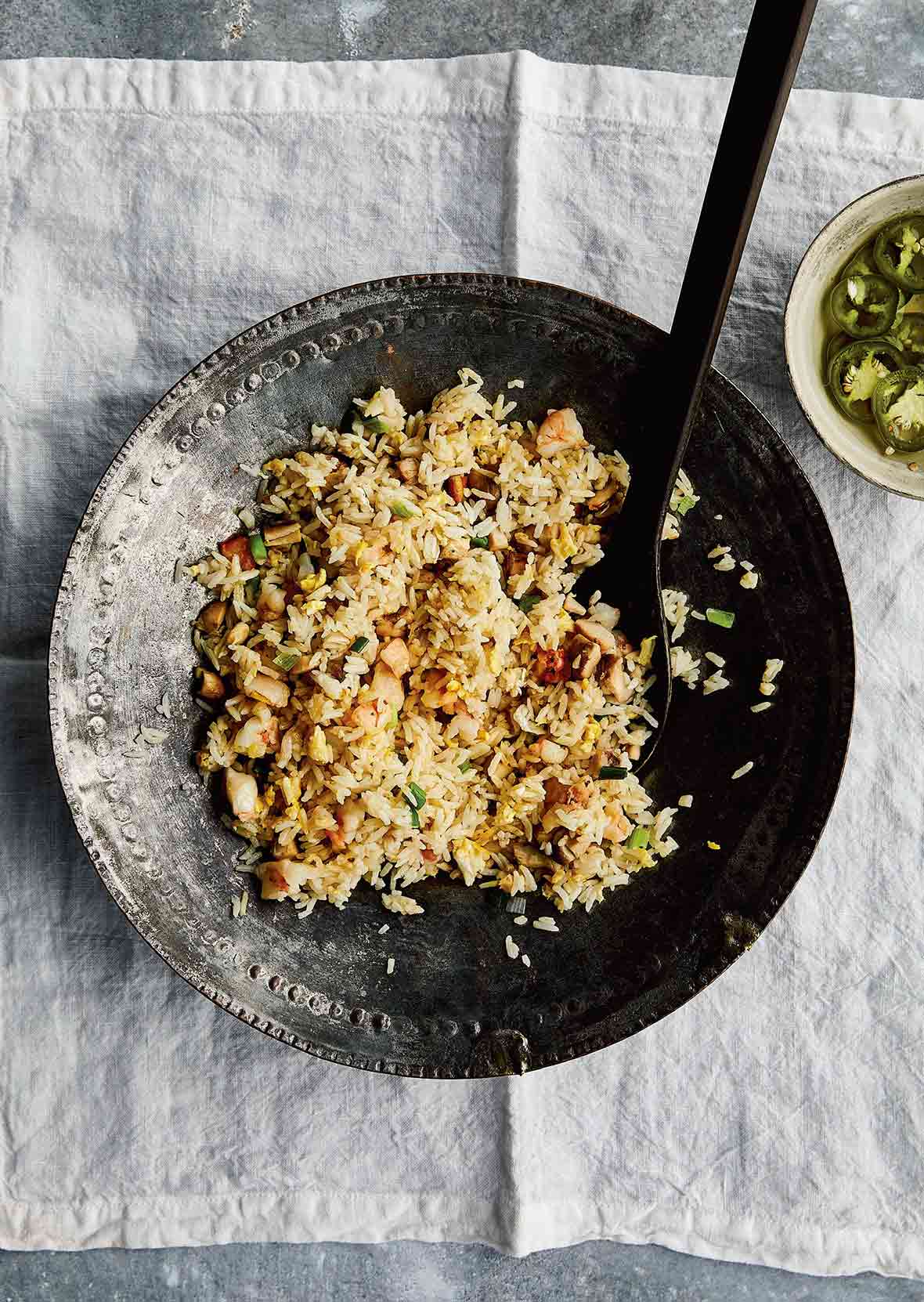 A decorative metal serving bowl filled with fried rice with leftovers and a bowl of jalapeño garlic vinegar on the side