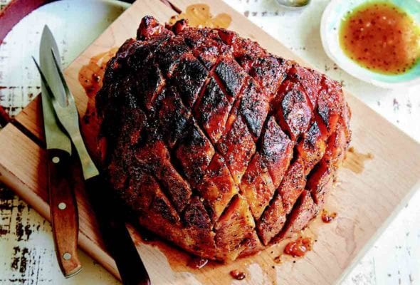 A fully cooked ham with ginger peach glaze on a carving board