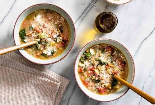 Two white bowls filled with lentil and escarole soup with a jar of olive oil on the side