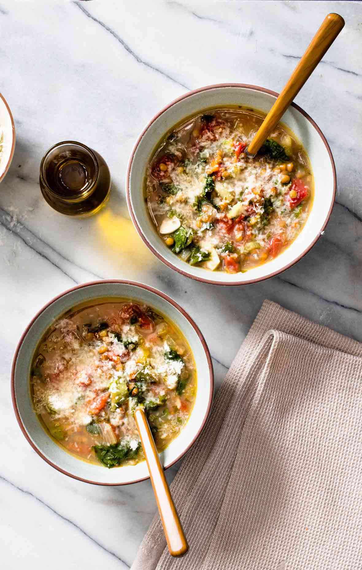 Two white bowls filled with lentil and escarole soup with a jar of olive oil on the side
