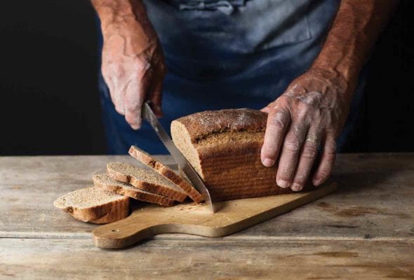 A man cutting a loaf of milk rye bread on a wooden board