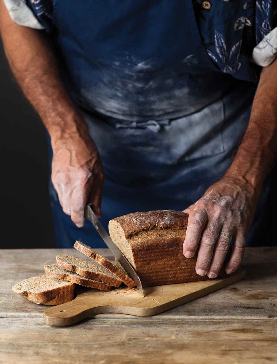 A man cutting a loaf of milk rye bread on a wooden board