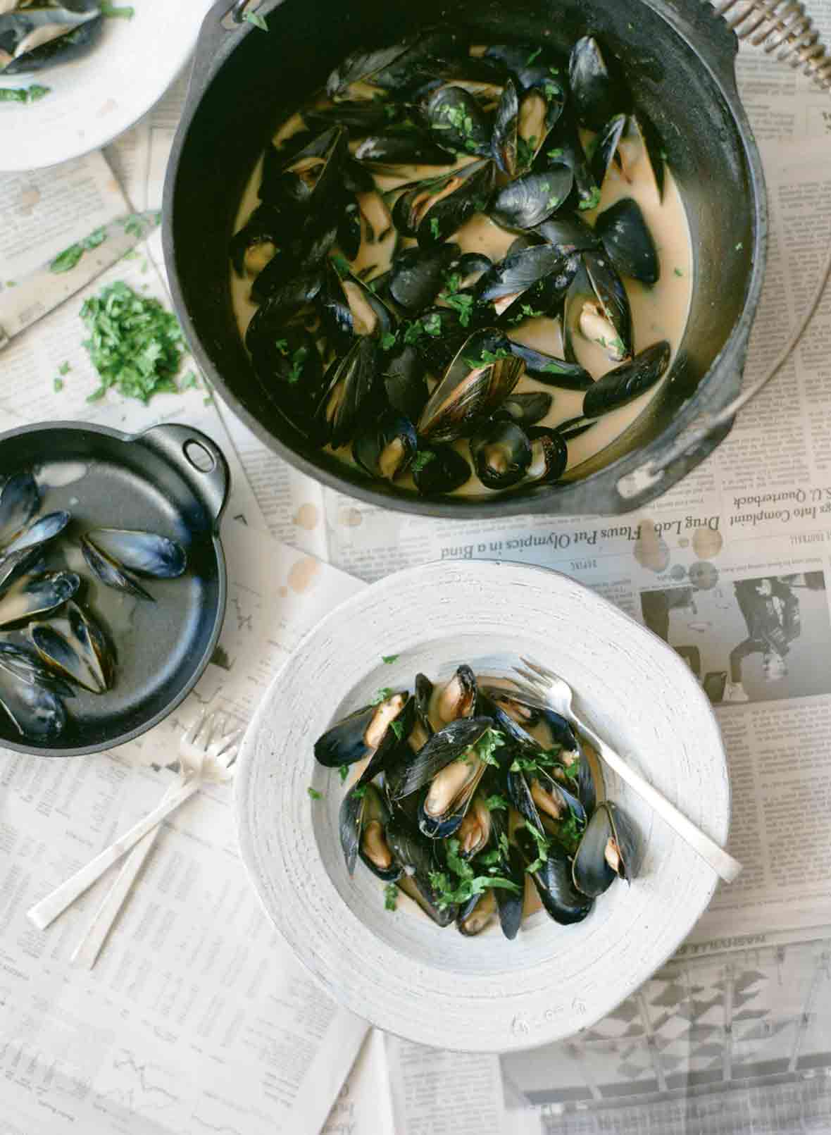 A pail and a white bowl filled with red curry mussels, as well as a bowl of discarded mussel shells